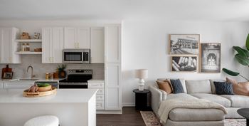 A modern kitchen with white cabinets and a grey sofa in the living room